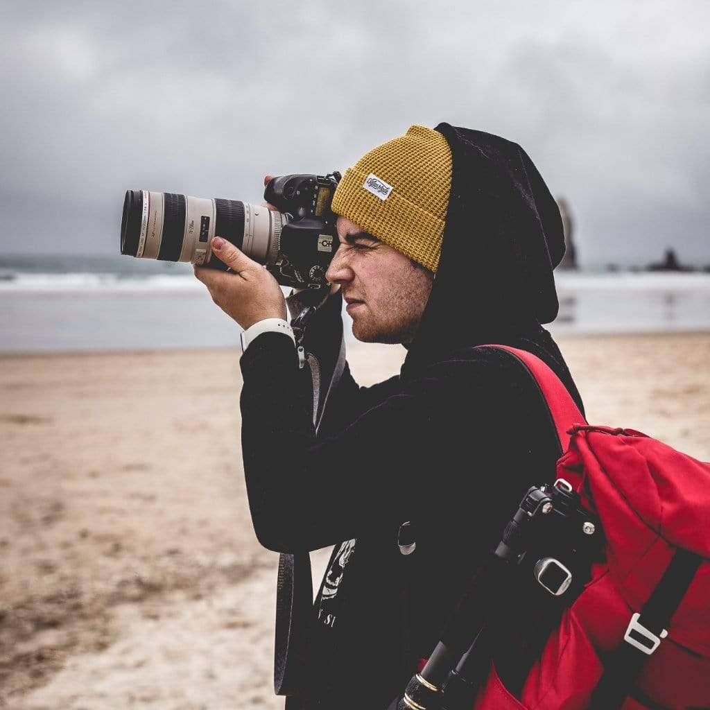 Yellow knit beanie with a brand logo on a wooden surface with a fireplace in the background